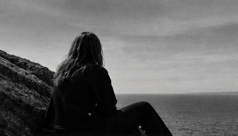 A figure seen from behind looking out over the sea